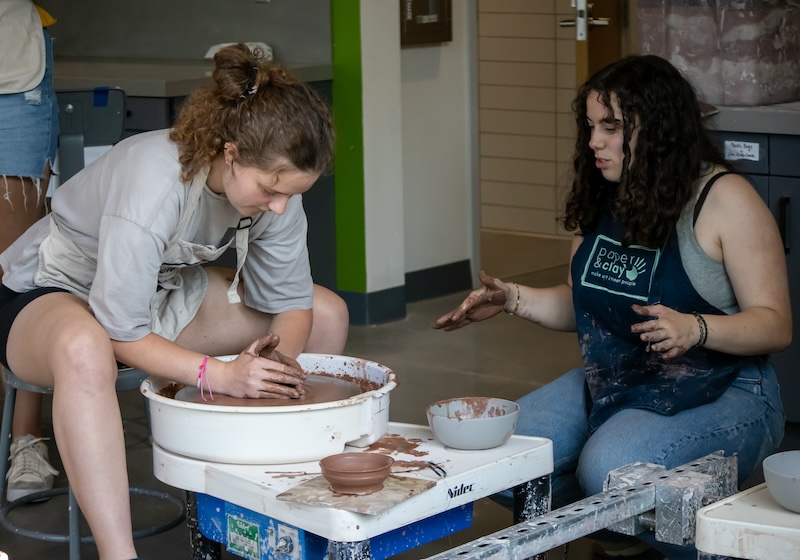 student making clay bowl with attendant guiding through process